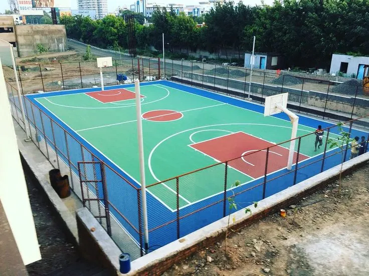Outdoor basketball court with green and red synthetic flooring, fenced area and professional markings