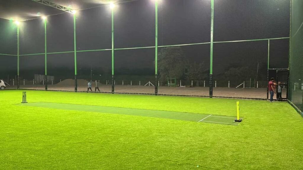 Outdoor box cricket turf with artificial grass, net fencing, and night lighting setup