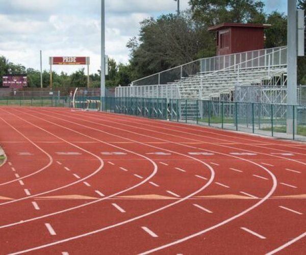 Outdoor acrylic jogging track with red surface, lane markings, and stadium seating