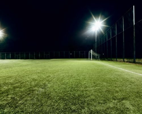 Outdoor football turf with artificial grass, goal post, fencing, and night flood lighting
