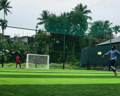 Players playing football on artificial turf ground with goal post and net fencing